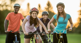 An image of four youth riding bicycles outside and wearing helmets.