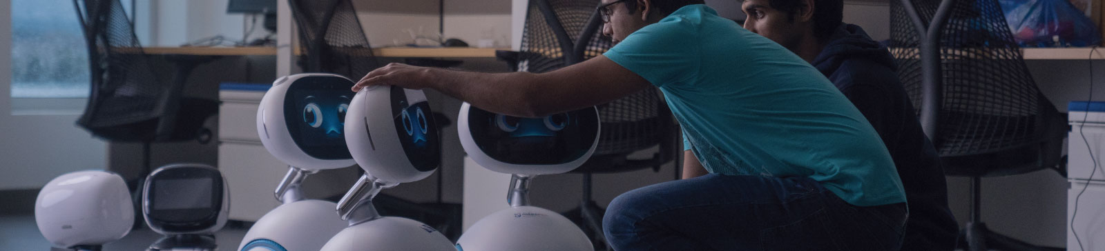 Students sitting on the floor interacting with small robots.