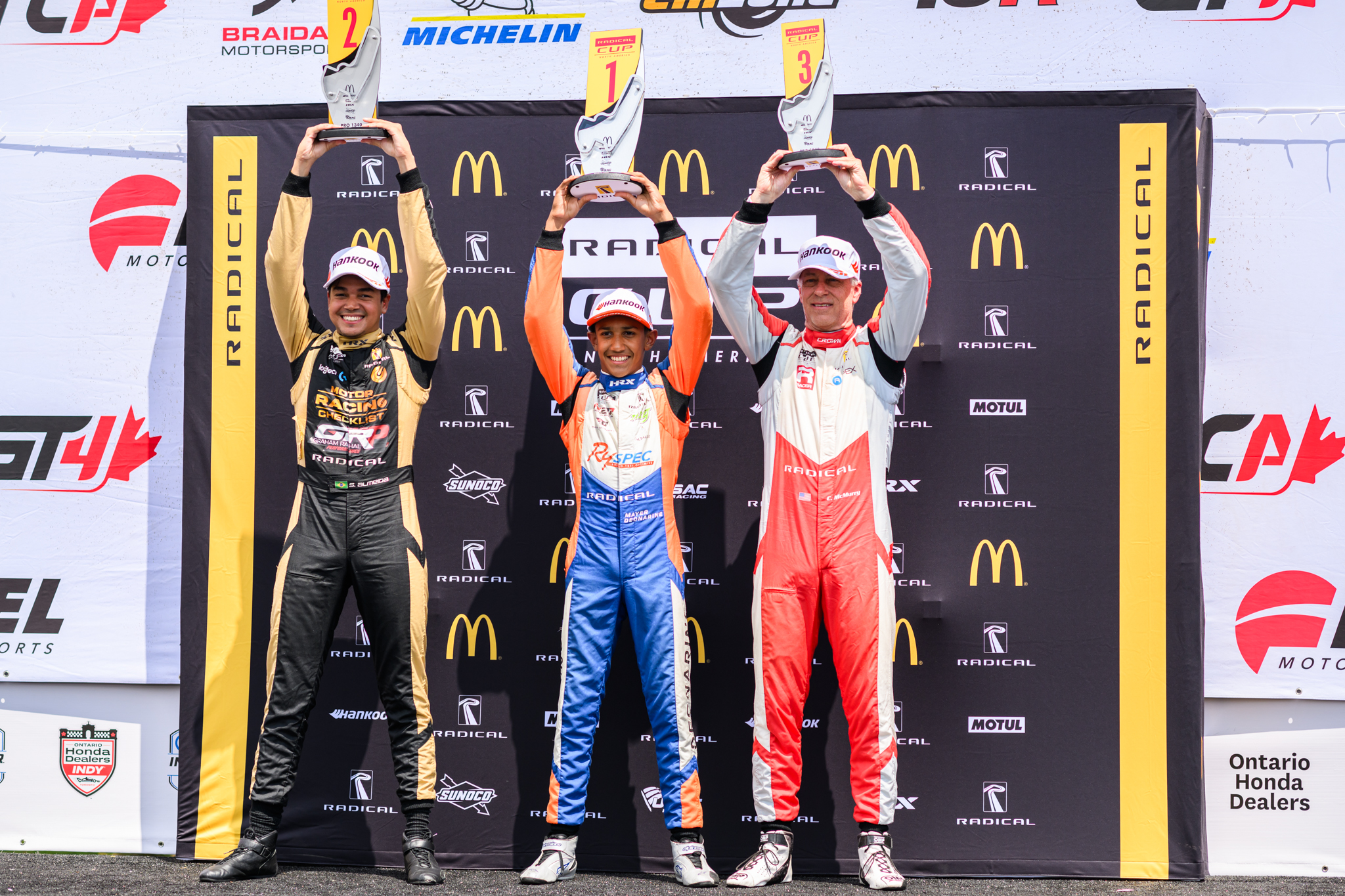 Mayer standing on the winners podium with two race car drivers