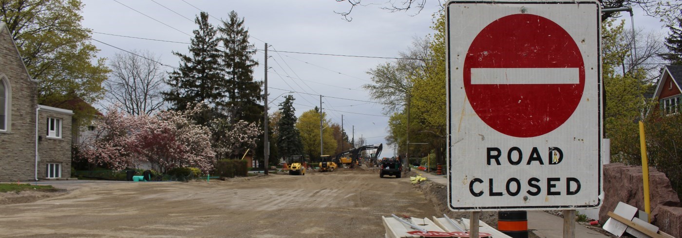 Road closure sign in front of construction vehicles performing road work