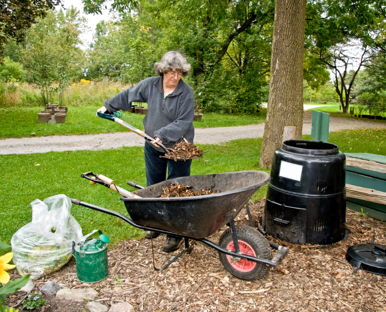Women adding leaves to a backyard composter