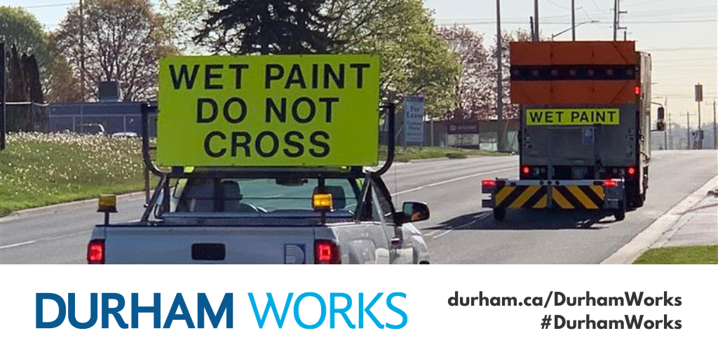 A photo of the back of two line painting vehicles with bright neon signs reading Wet Paint Do Not Cross and Wet Paint with a Durham Works logo banner and text reading durham.ca/DurhamWorks #DurhamWorks 