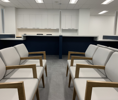 An image of chairs in the foreground featuring a service counter with cupboards in the background. 