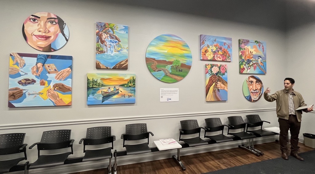 Art collection at 200 John Street. An image of various art pieces on a wall with an artist beside