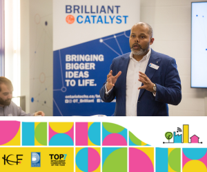 A person speaking to an audience, with a stand-up banner behind them that reads, "Bringing Bigger Ideas to Life."