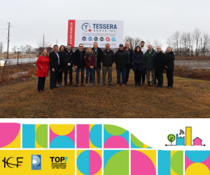 A group of people posing at a construction site for a new business announcement with a Tessera Group sign behind them. 