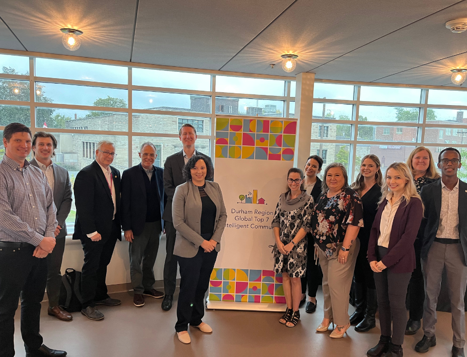 A photo of the Intelligent Communities Forum smiling, standing in front of a banner that reads. Top7 Intelligent Communities of the Year.