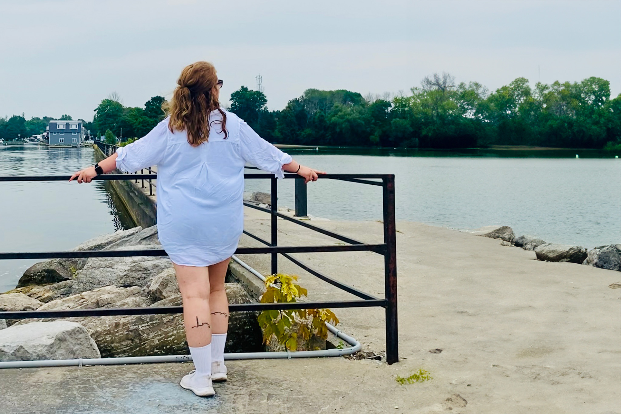 Person stands on pier with back to camera taking in the views of the water