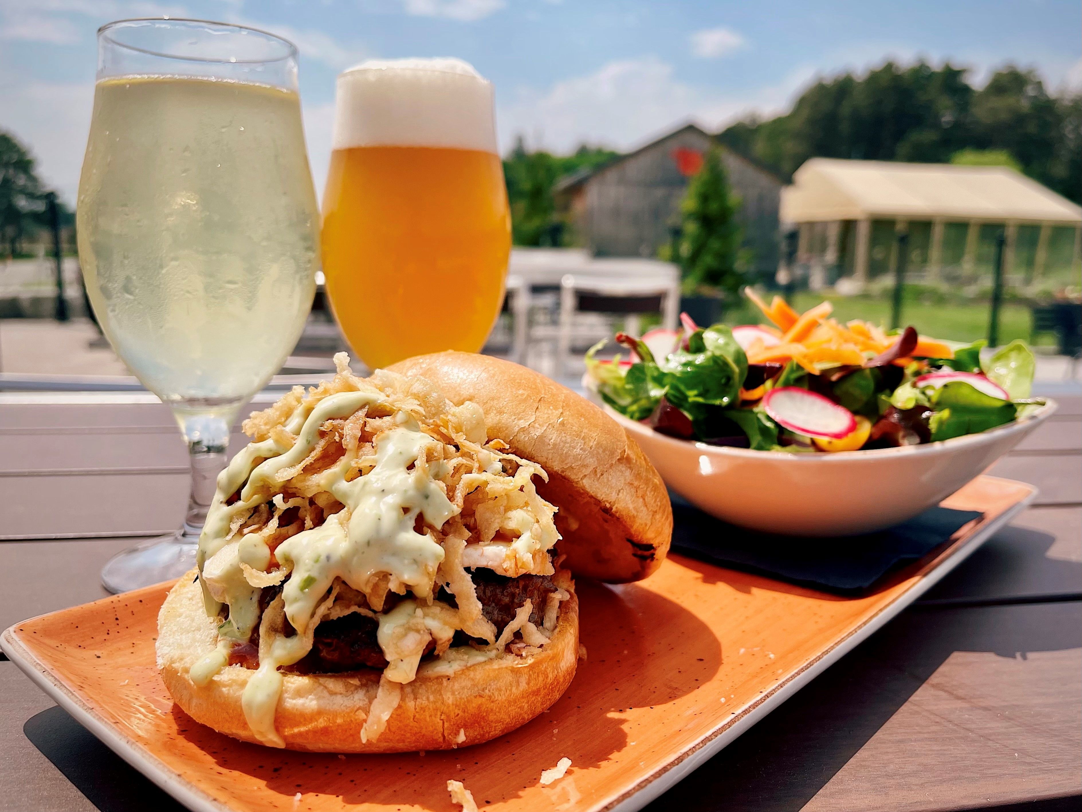 Image of a bison burger from Slabtown Cider on a picnic table with a glasses of cider and beer in the background