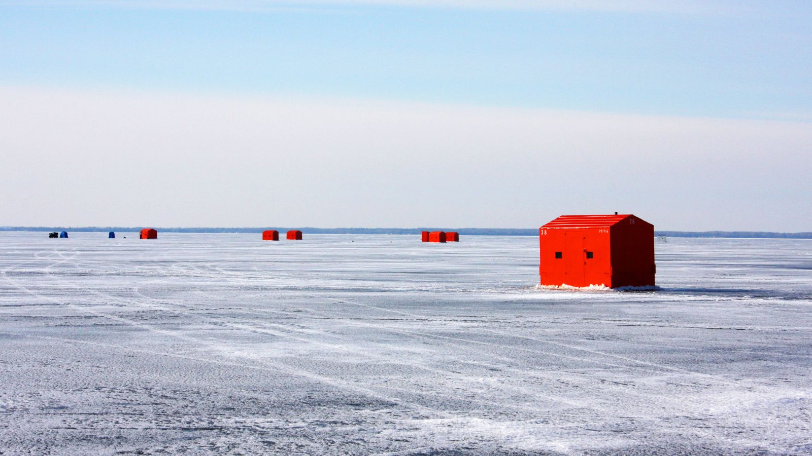 Image of several red ice fishing huts on a frozen lake