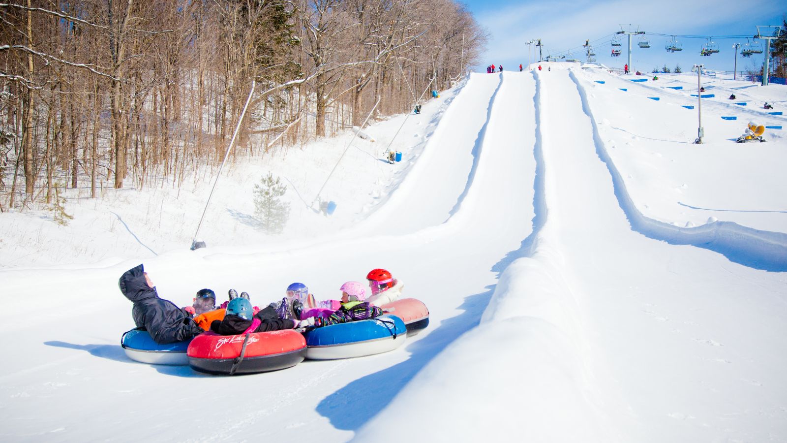 Image of a group of people going down a hill on snow tubes