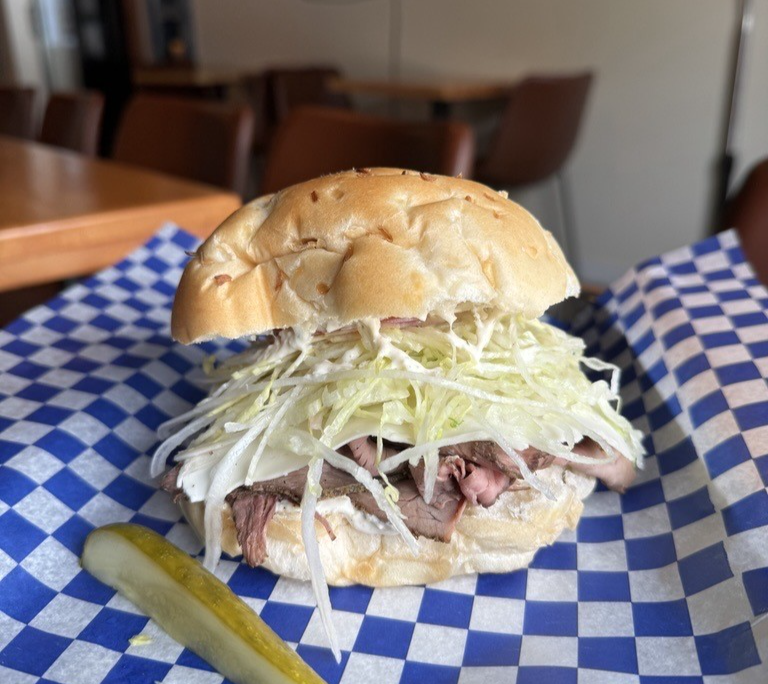 Image of a roast beef sandwich served on a tray with a pickle on the side