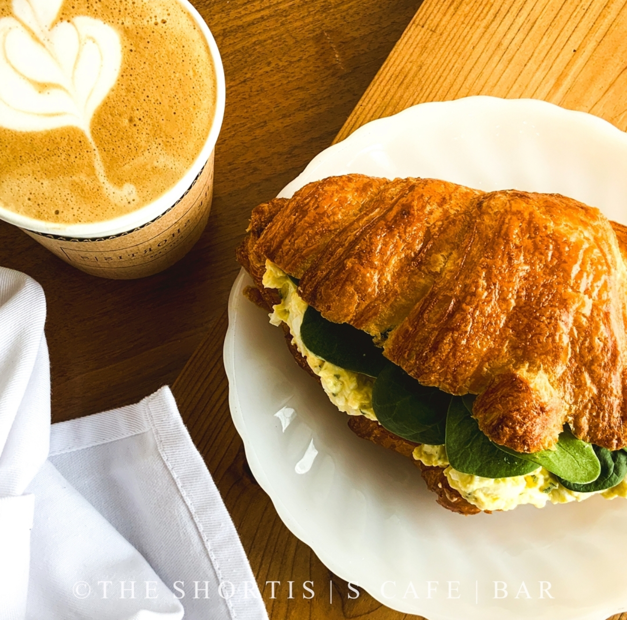 Aerial image of a sandwich served on a croissant beside a coffee with latte art