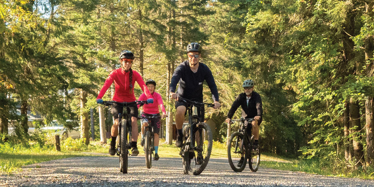 A group of cyclists biking on a path surrounded by trees.