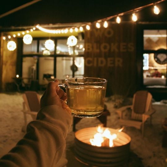 Hand holding a glass of cider by an outdoor firepit at Two Blokes Cider in Scugog, Ontario