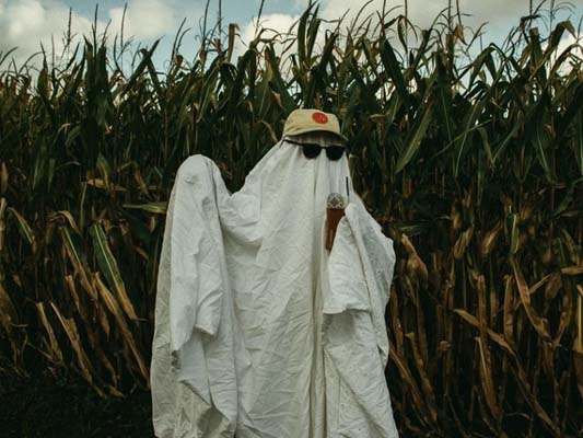 Person in a ghost costume in front of a corn field.