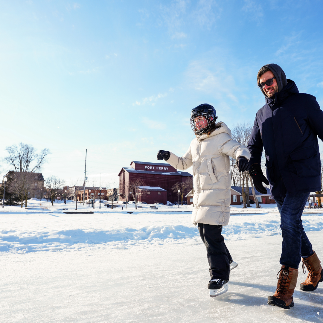 Image of two people skating on a frozen lake with a small town main street in the background