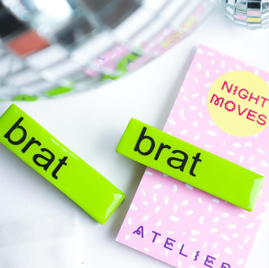 Image of hair clips in chartreuse green on a backer card that says Night Moves Atelier. The clips say Brat in black text.