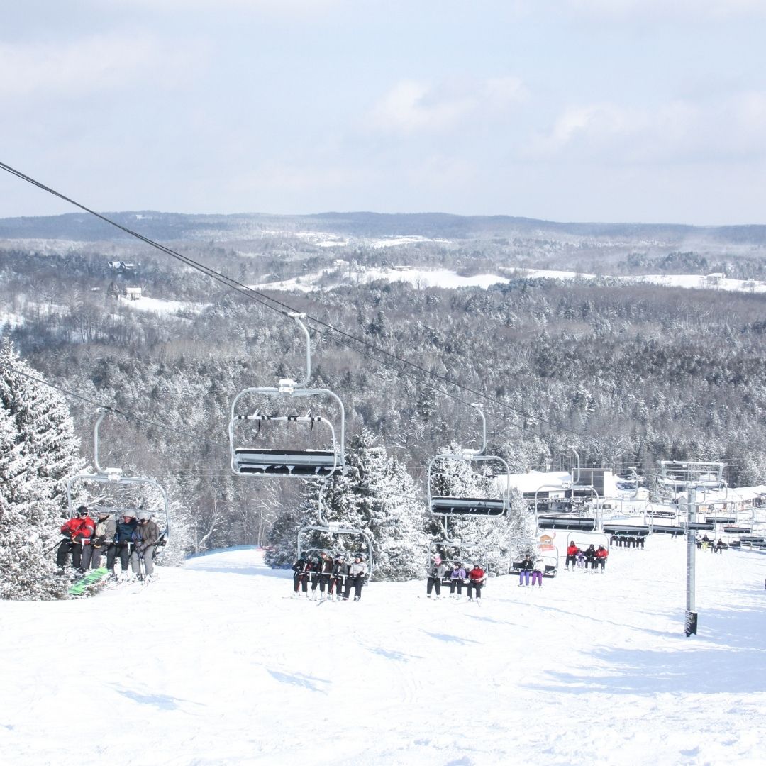 Image of a chair lift full of skiers and snowboarders with beautiful winter scenery in the background