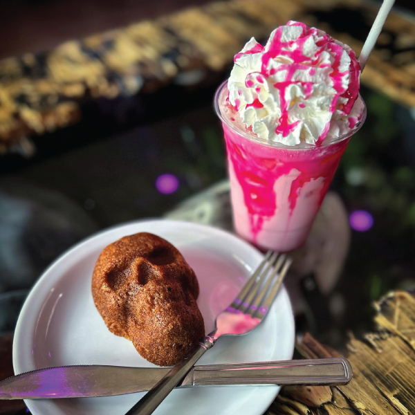 Deadly Grounds chilled pink drink with whipped cream and a skull shaped muffin on a plate.