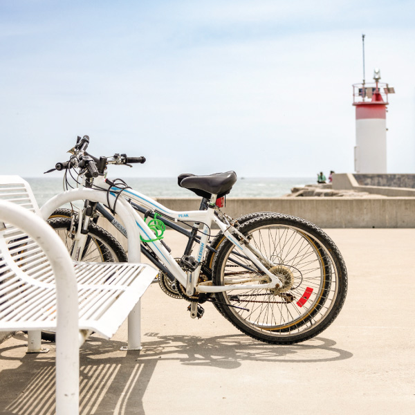 Bikes parked along the waterfront with a lighthouse in the background on a summer day.