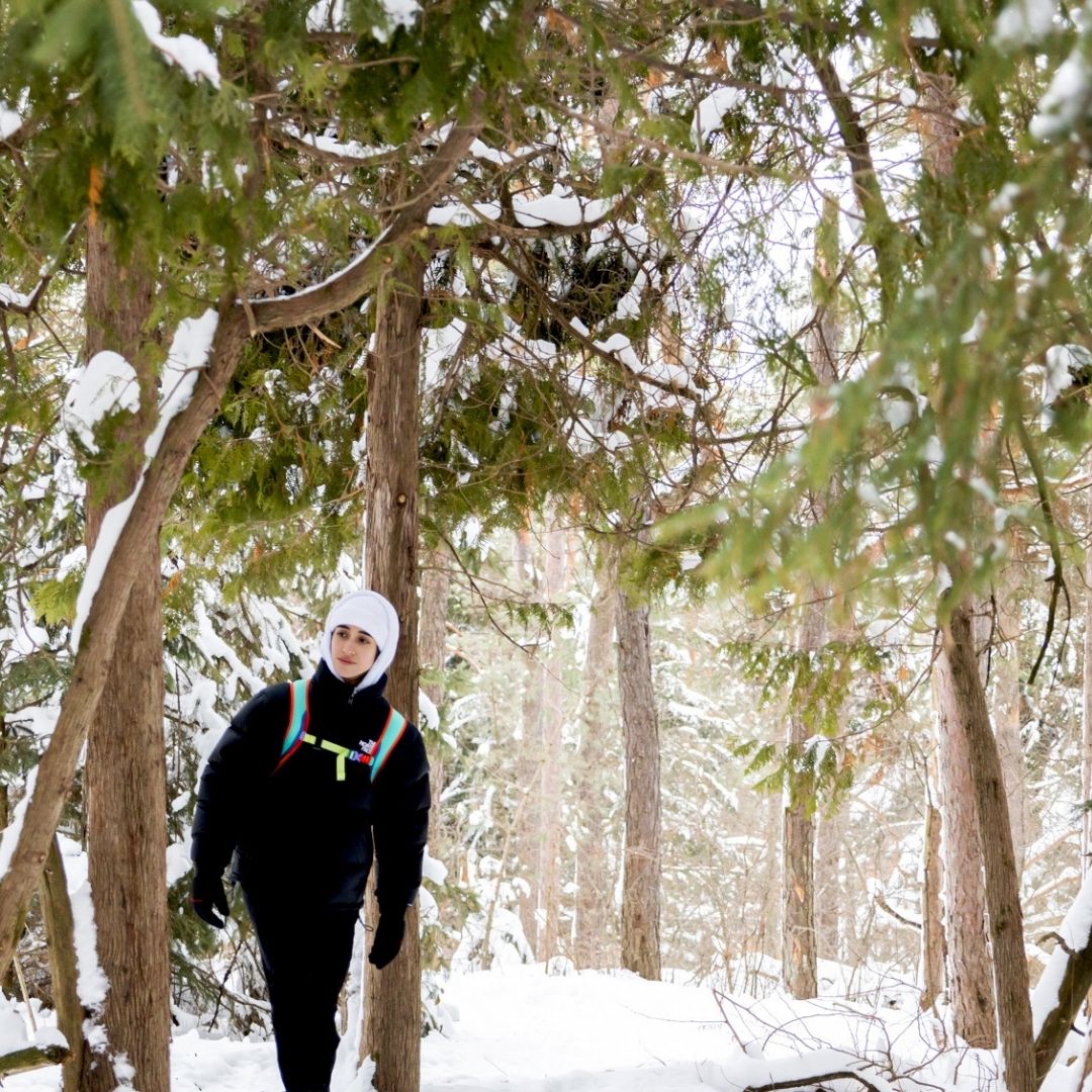 A young person walks through a forest in the winter