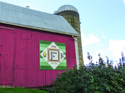 Quilt design in a square hanging from the side of a red barn.