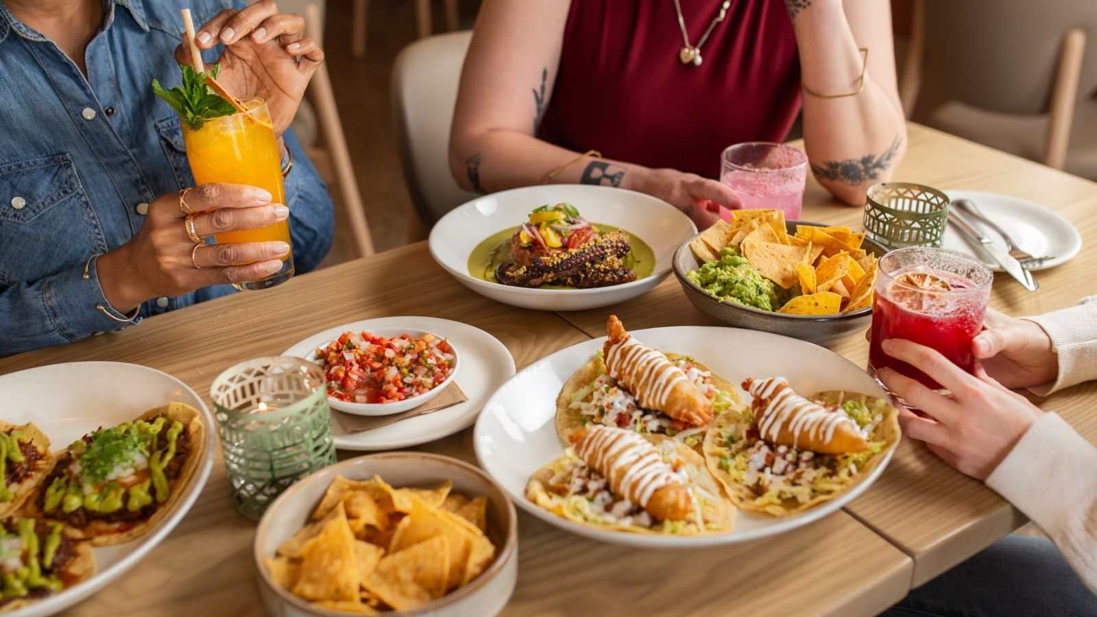 Image of three friends sitting around a table full of dishes, enjoying cocktails at a Mexican restaurant