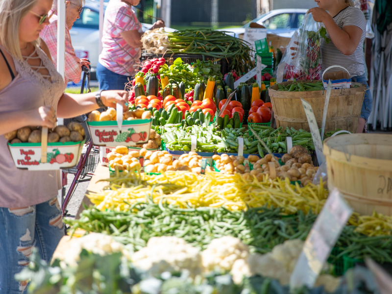 A display of vegetables at a farmers' market with people shopping in the background