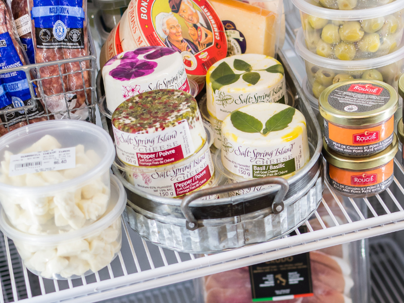 Image of the inside of a fridge at a gourmet food shop full of cheese, charcuterie, and olives