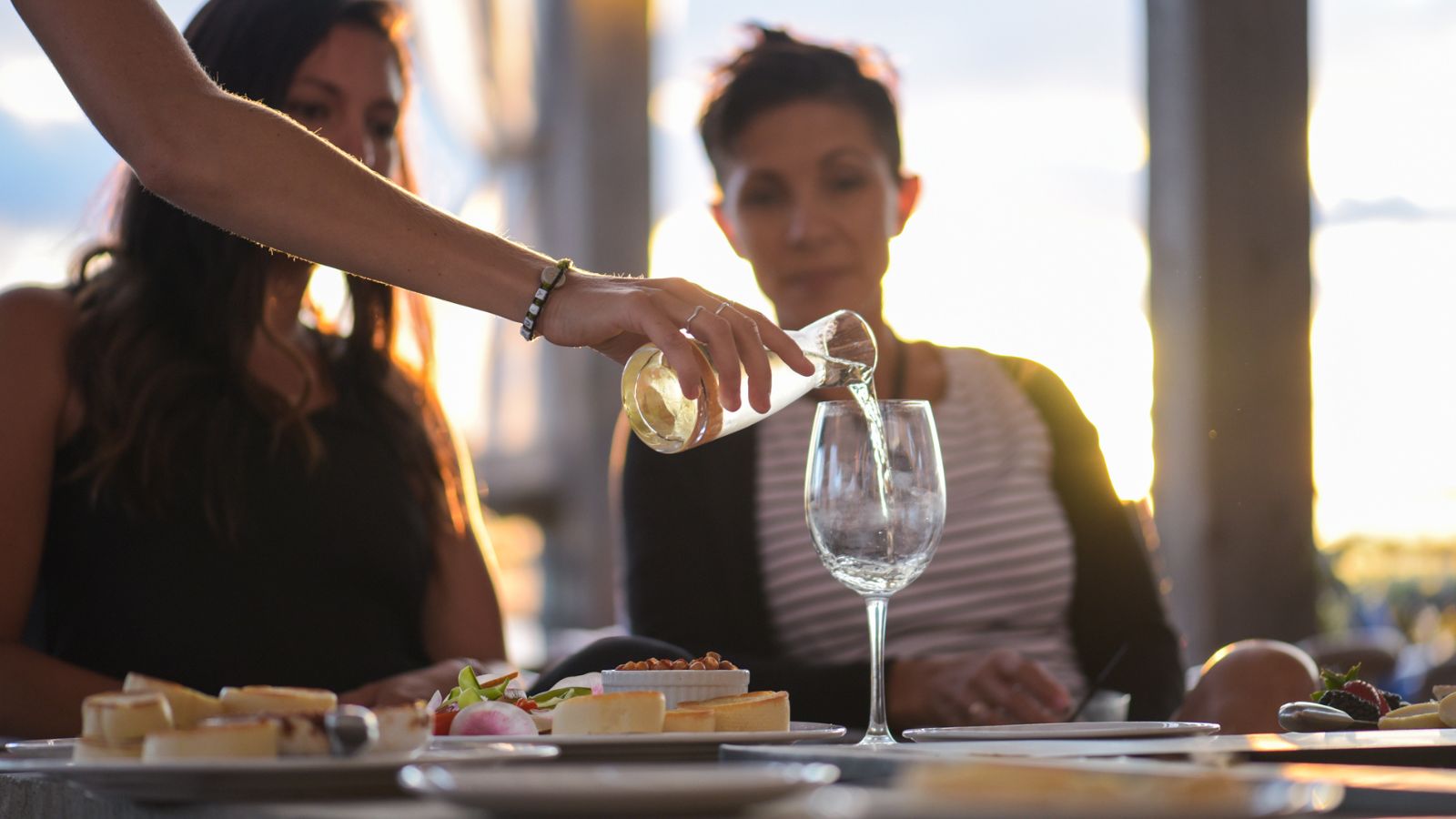 Two people sitting at a restaurant table and a server is pouring them a glass of wine