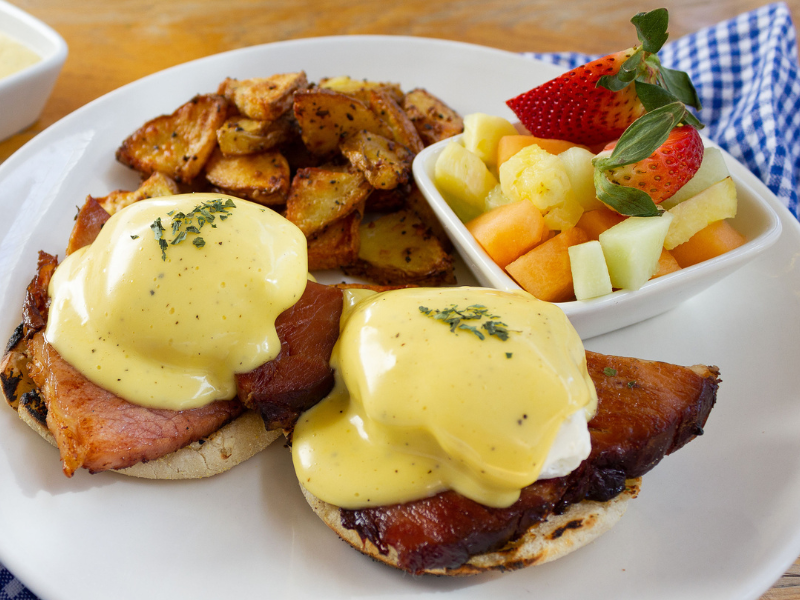 Eggs benedict topped with rich hollandaise, home fries, and fresh fruit.