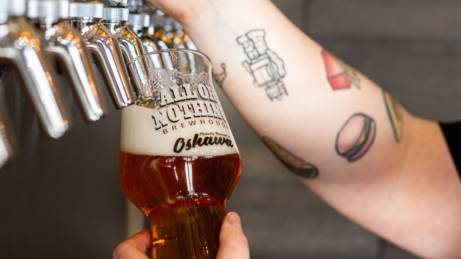 A tattooed bartender pours an amber ale into a pint glass