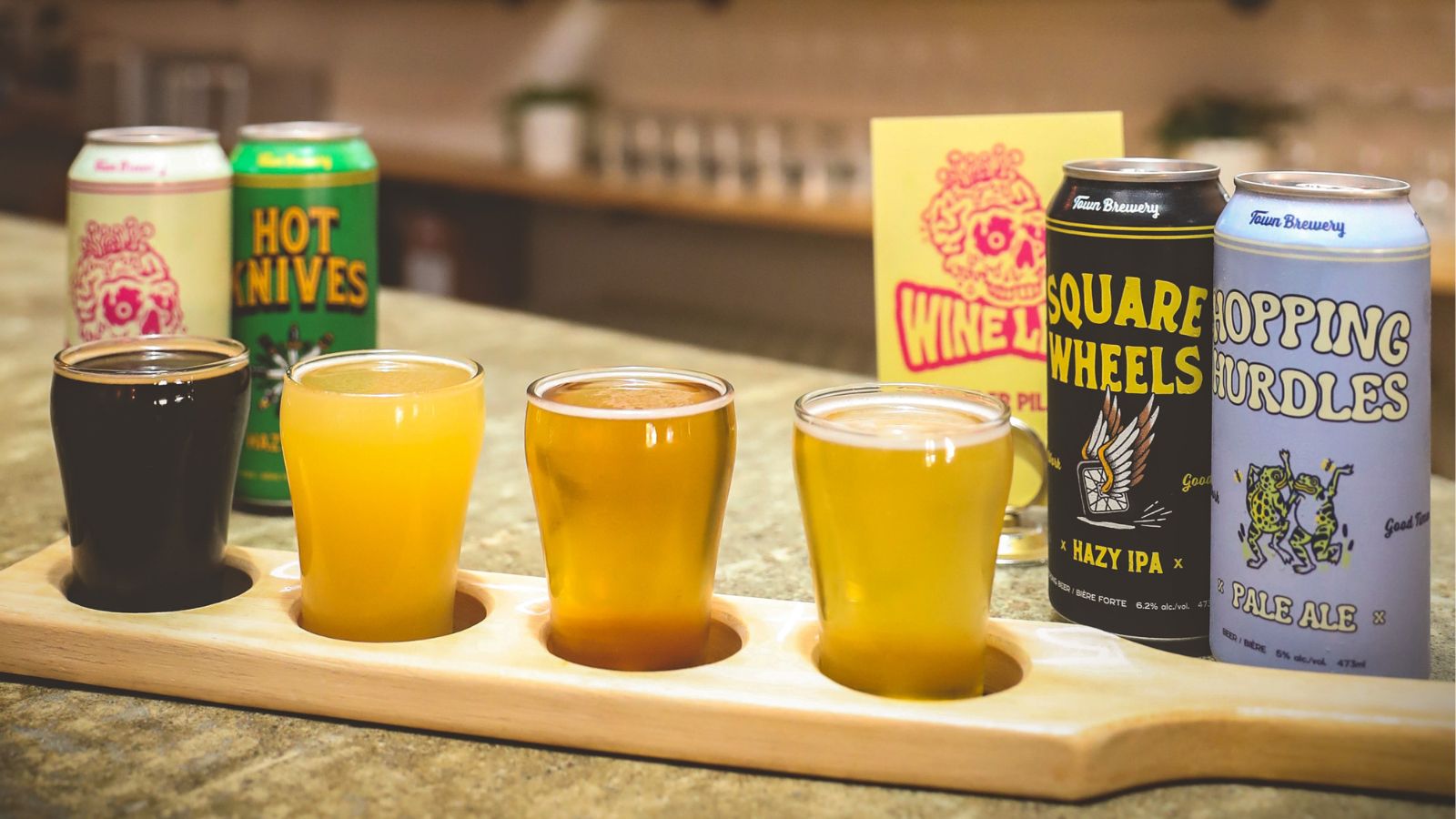 Image of a tasting flight of beer on a wooden paddle with cans of beer on either end of it