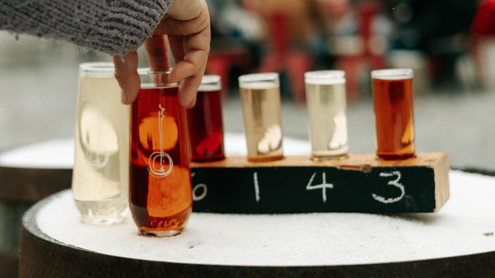 Image of a tasting flight of cider on a snowy table with a hand reaching in to grab a glass