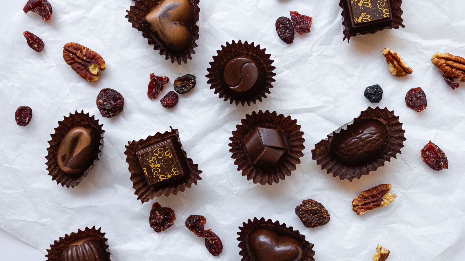 Image of gourmet chocolates scattered on a white surface with different ingredients surrounding them 