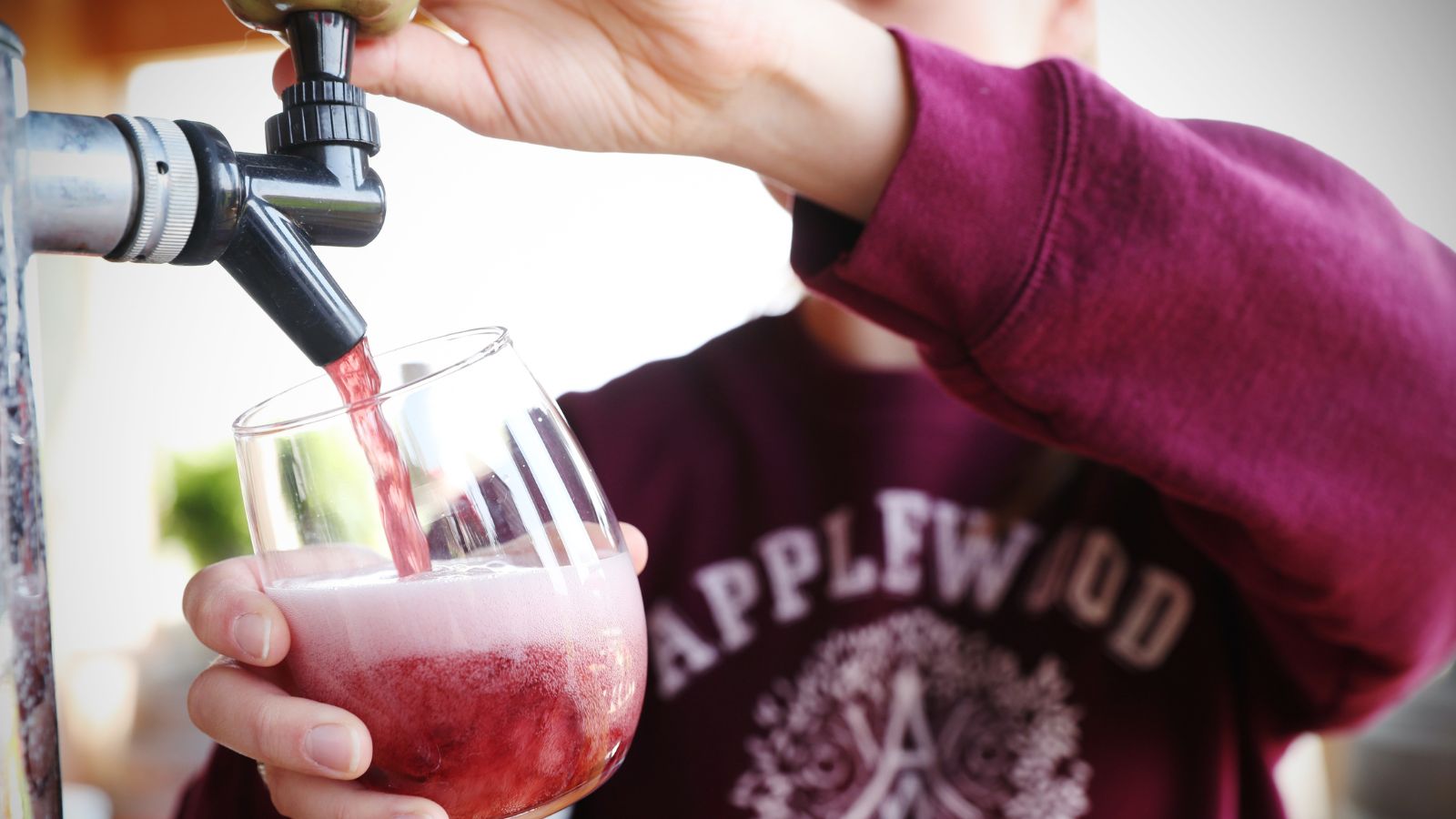 Image of a bartender pouring a pretty pink fruit wine from a tap into a wine glass