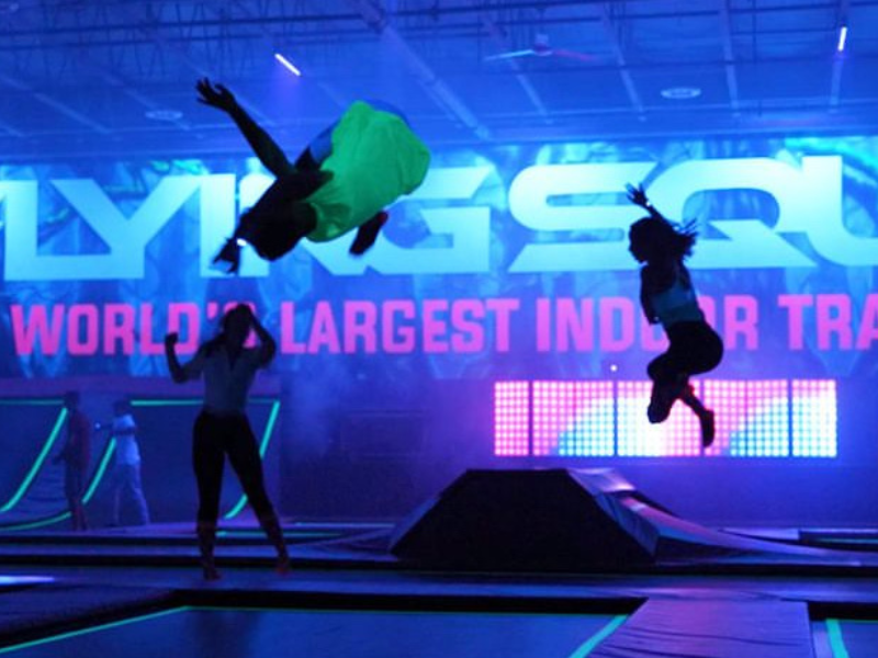 Three children jumping on trampolines in indoor playground which is lit with black lights