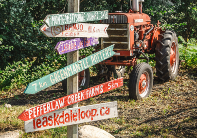 A sign post in front of a tractor with signs pointing to stops on a trail of rural businesses