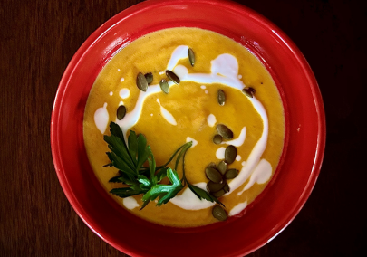 Aerial image of a red bowl of carrot soup garnished with coconut cream and herbs